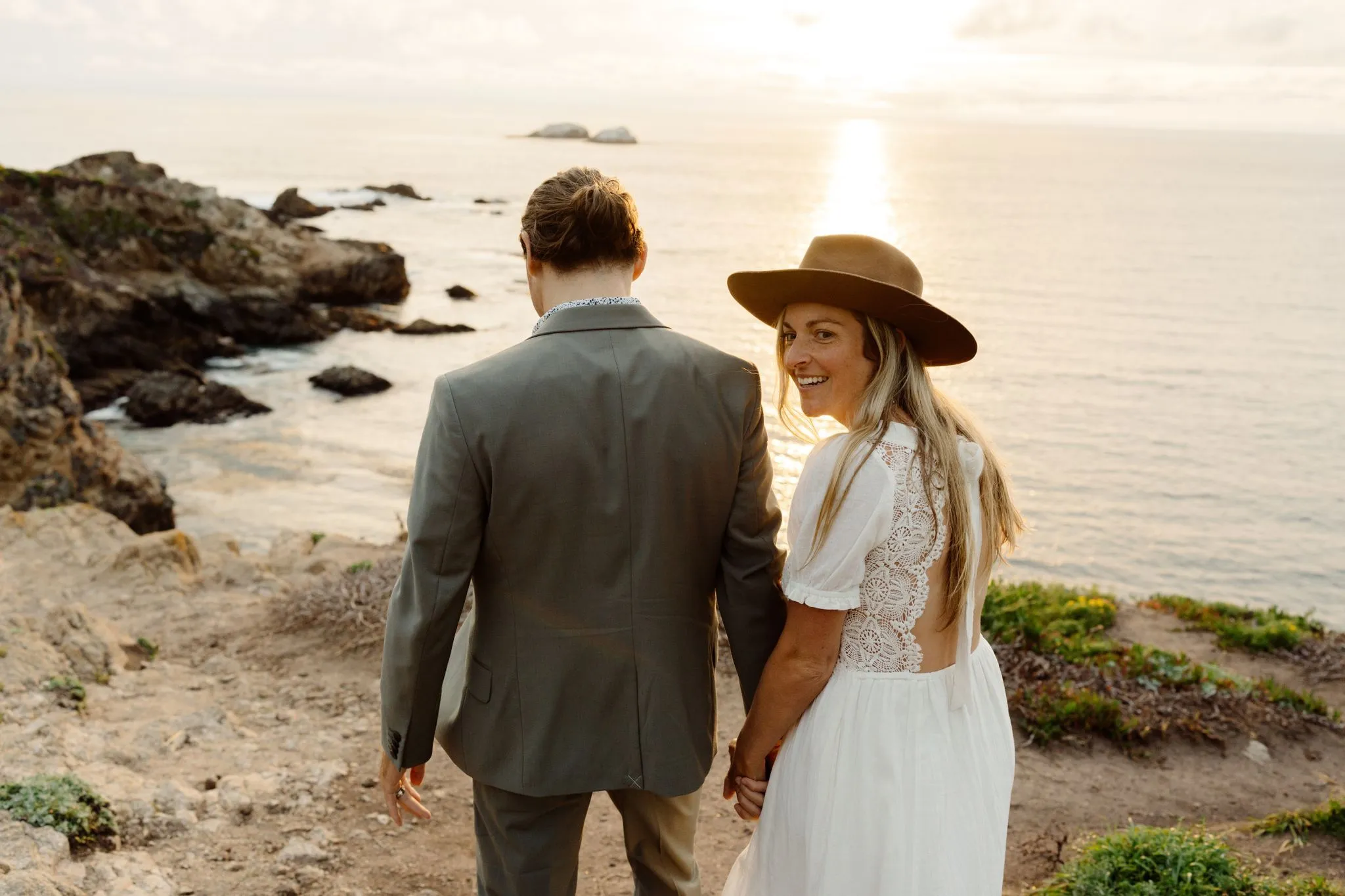 A couple holding hands and walking together along a coastal cliff at sunset