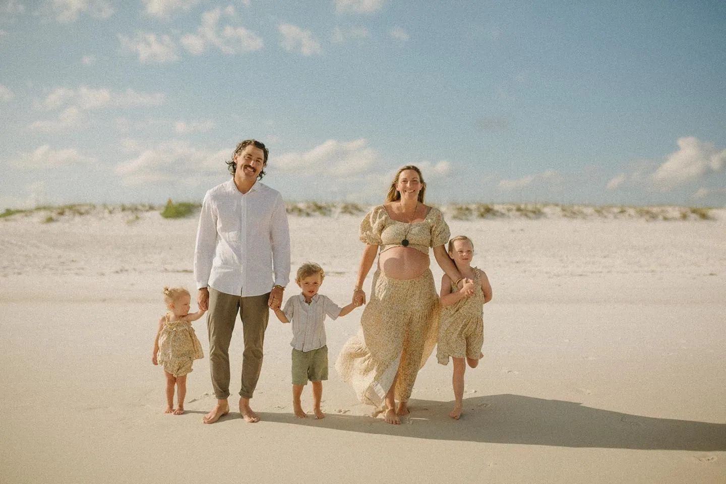 The whole Aliff family walking hand in hand across an open stretch of white sand beach
