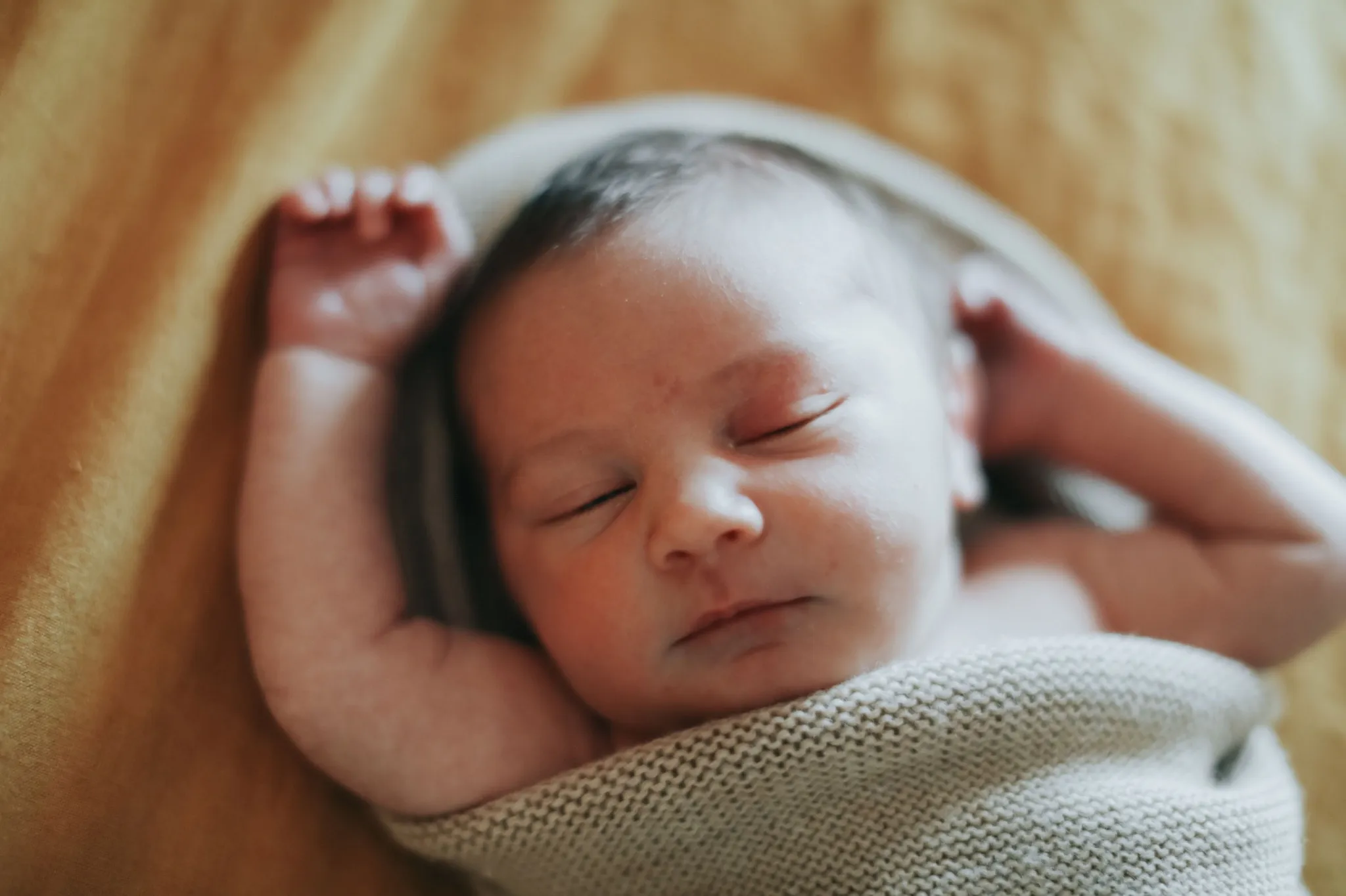 Newborn Jude swaddled in a cream knit blanket, both hands tucked up beside his face, asleep